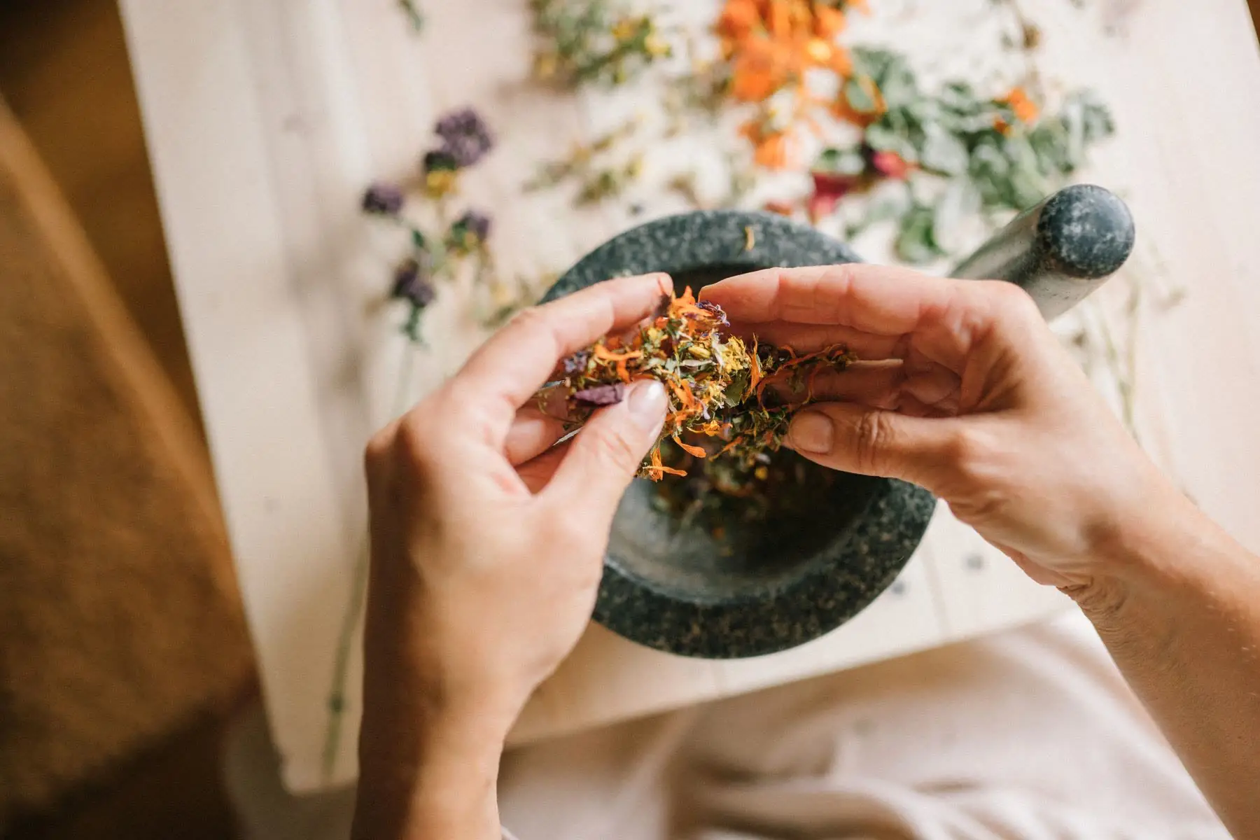 Hands crumbling dried herbs into a mortar